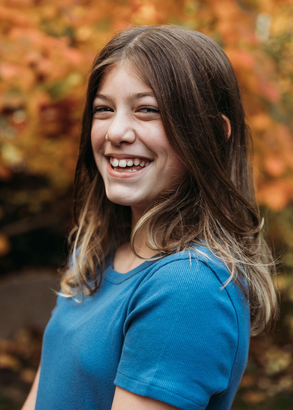 A joyful laugh captured against vibrant autumn foliage wearing a bright blue t-shirt.