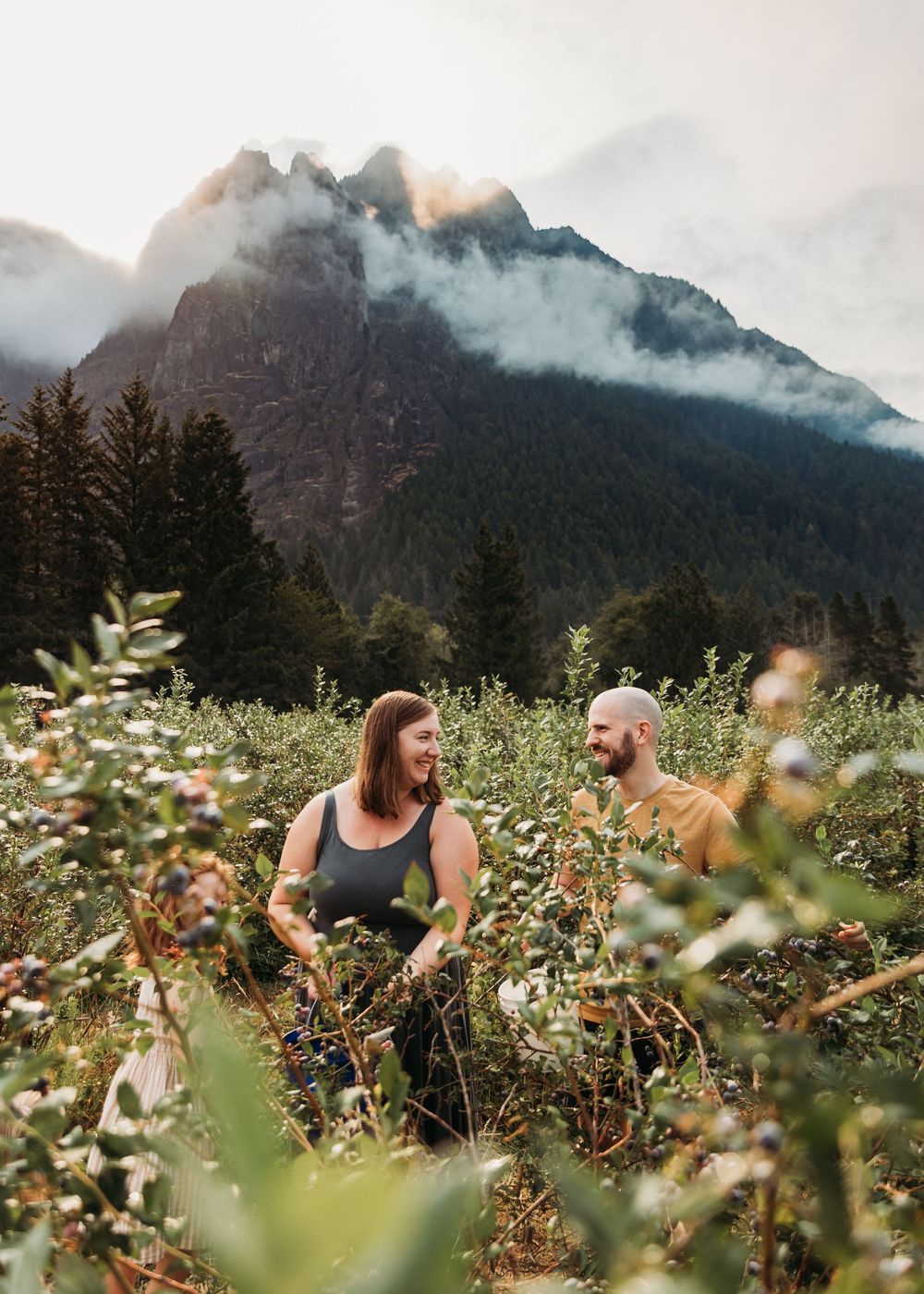 A couple enjoying time together in a wildflower meadow with misty mountains in the background near sunset.