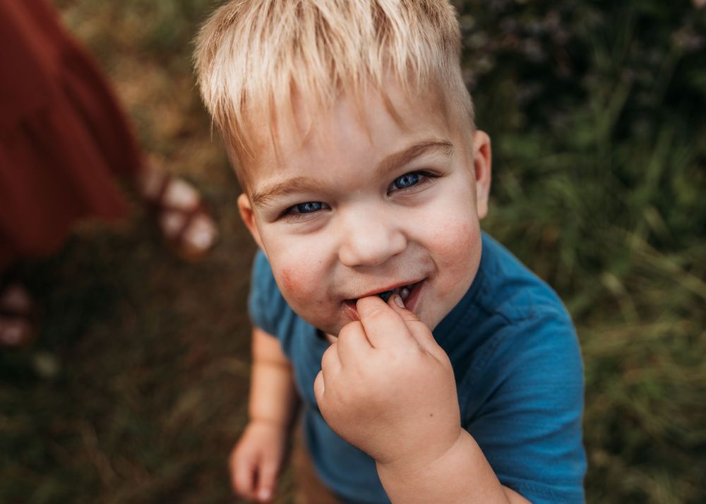 Young child in blue shirt smiling and laughing while playing outdoors in natural setting.