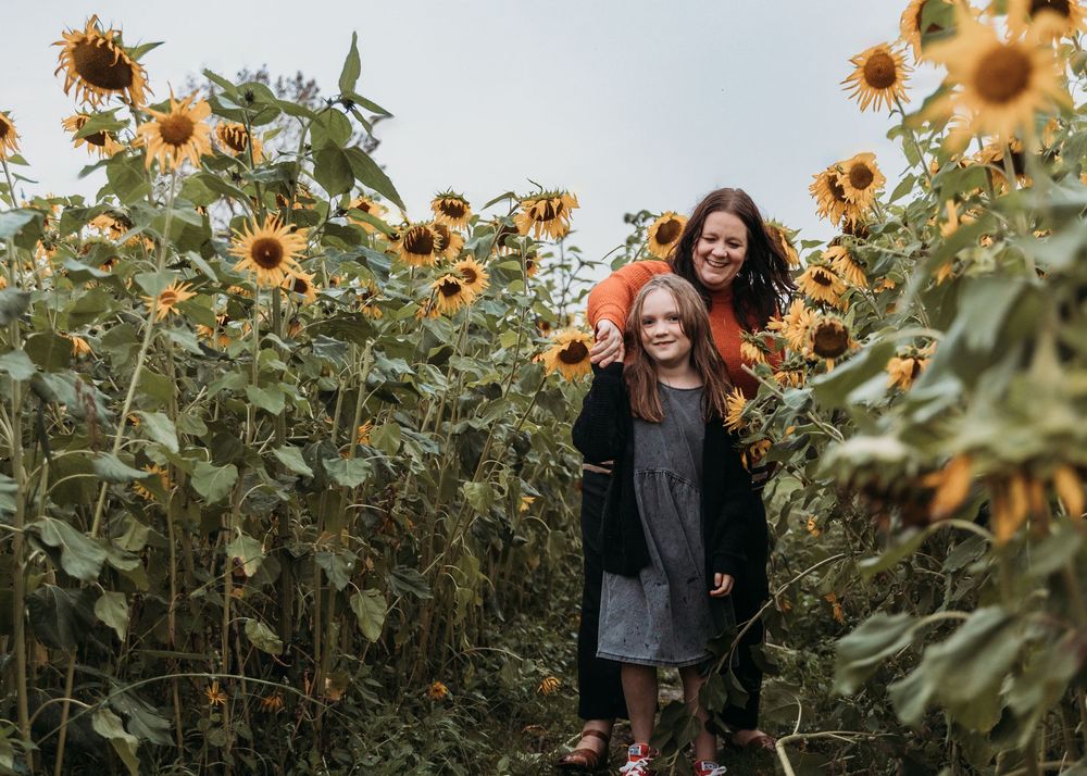 Two people standing together among tall blooming sunflowers in a garden during golden hour.