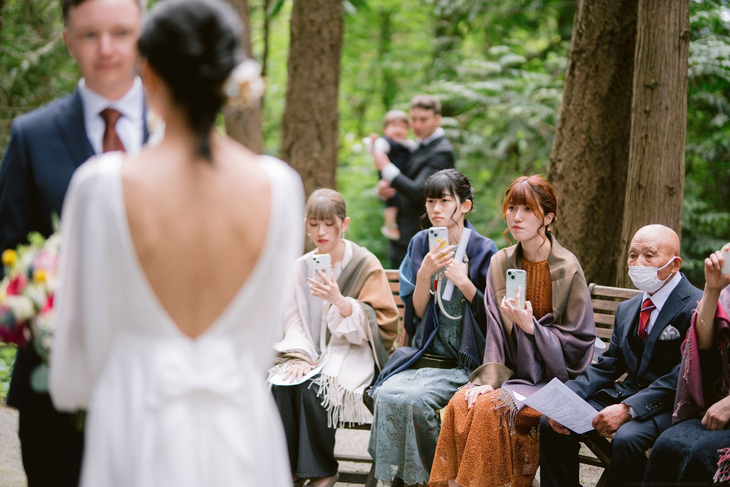 Wedding guests react with joy and applaud during an outdoor forest ceremony.