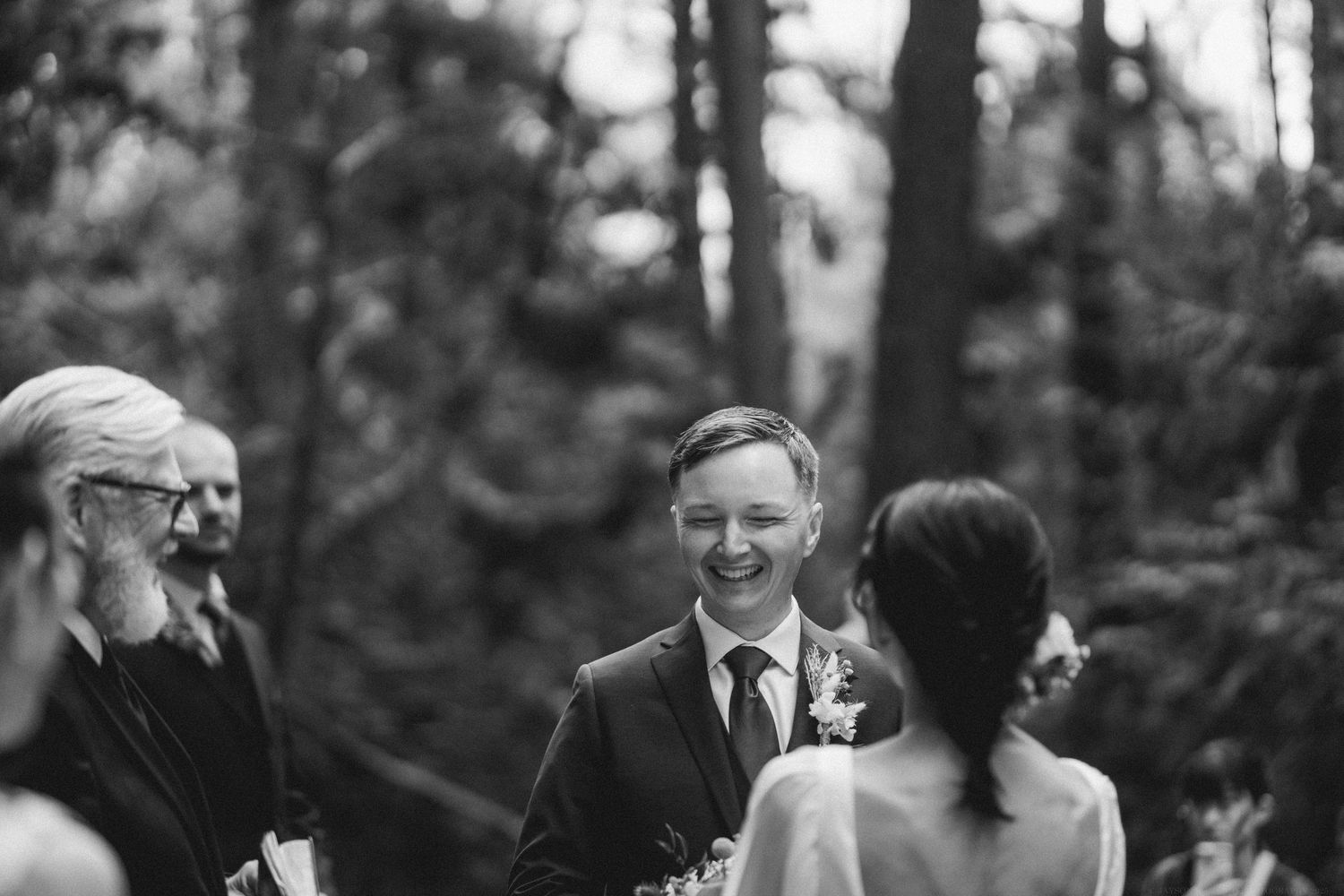 Black and white photo of an intimate outdoor wedding ceremony in a wooded forest setting.