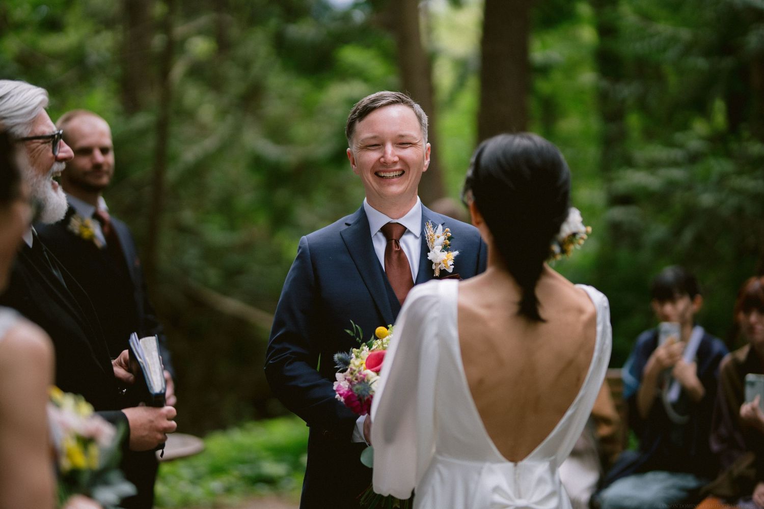 A joyful outdoor wedding ceremony in a lush forest setting with the couple exchanging vows among guests.
