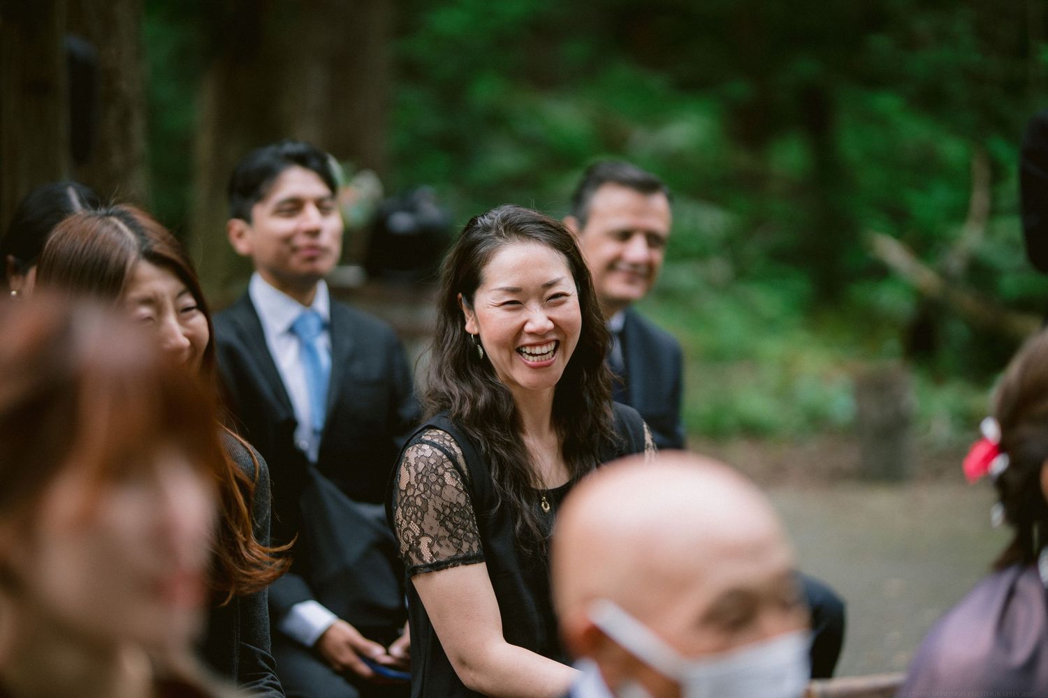 Wedding guests enjoying outdoor forest ceremony with joyful expressions.