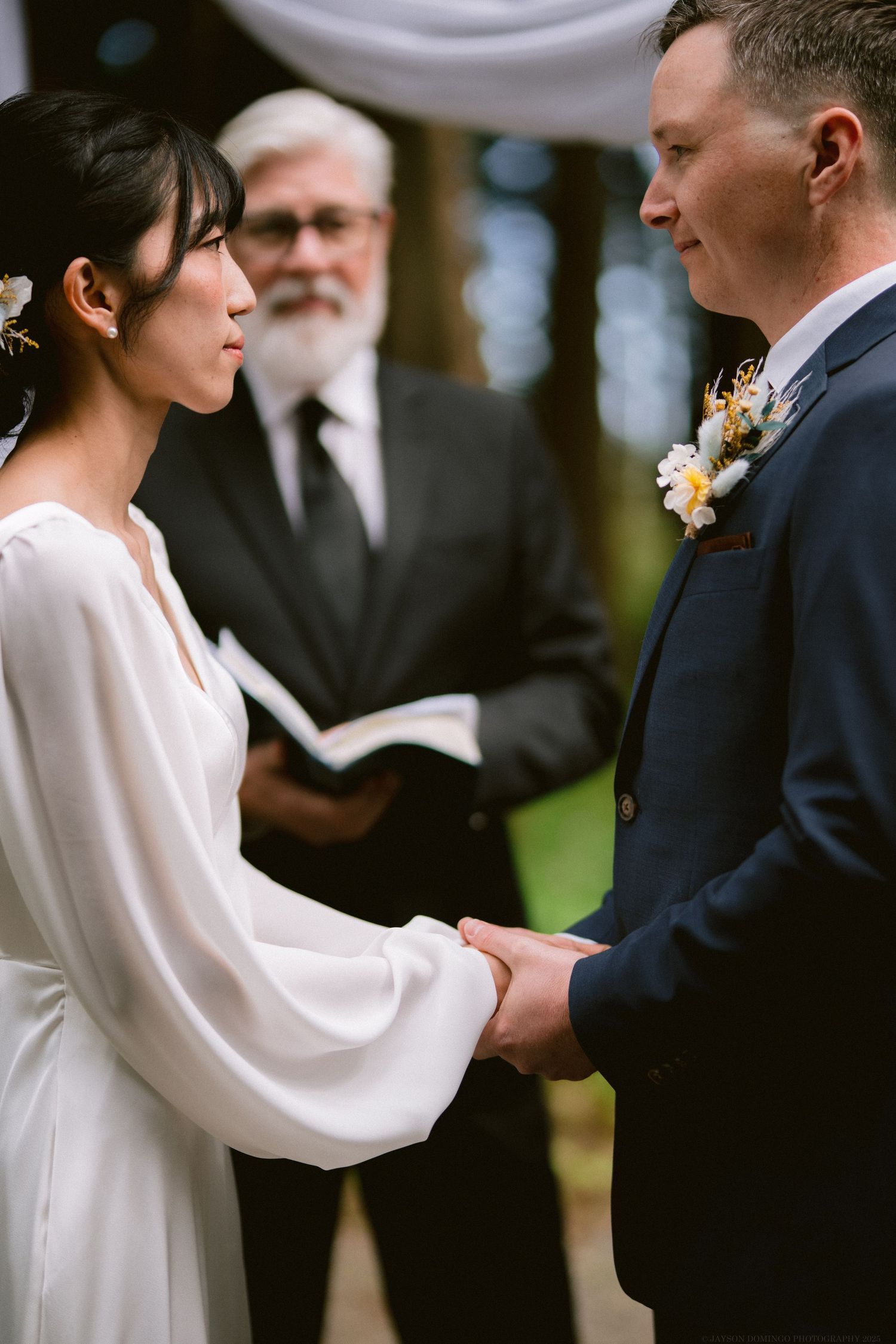 A couple exchanges vows during an intimate outdoor wedding ceremony with an officiant in the background.