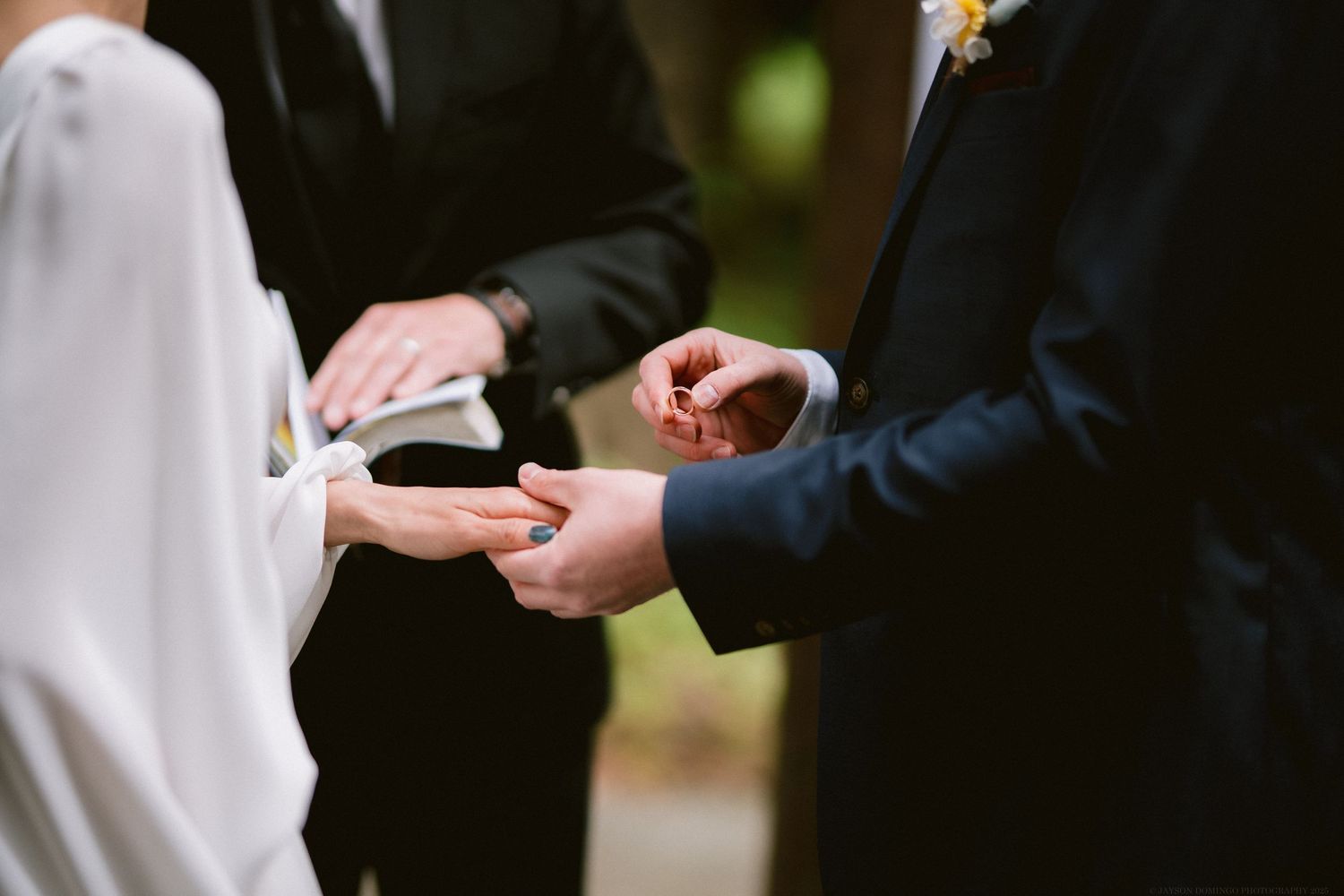 Close-up of hands during a wedding ceremony as rings are exchanged between couple against blurred background.