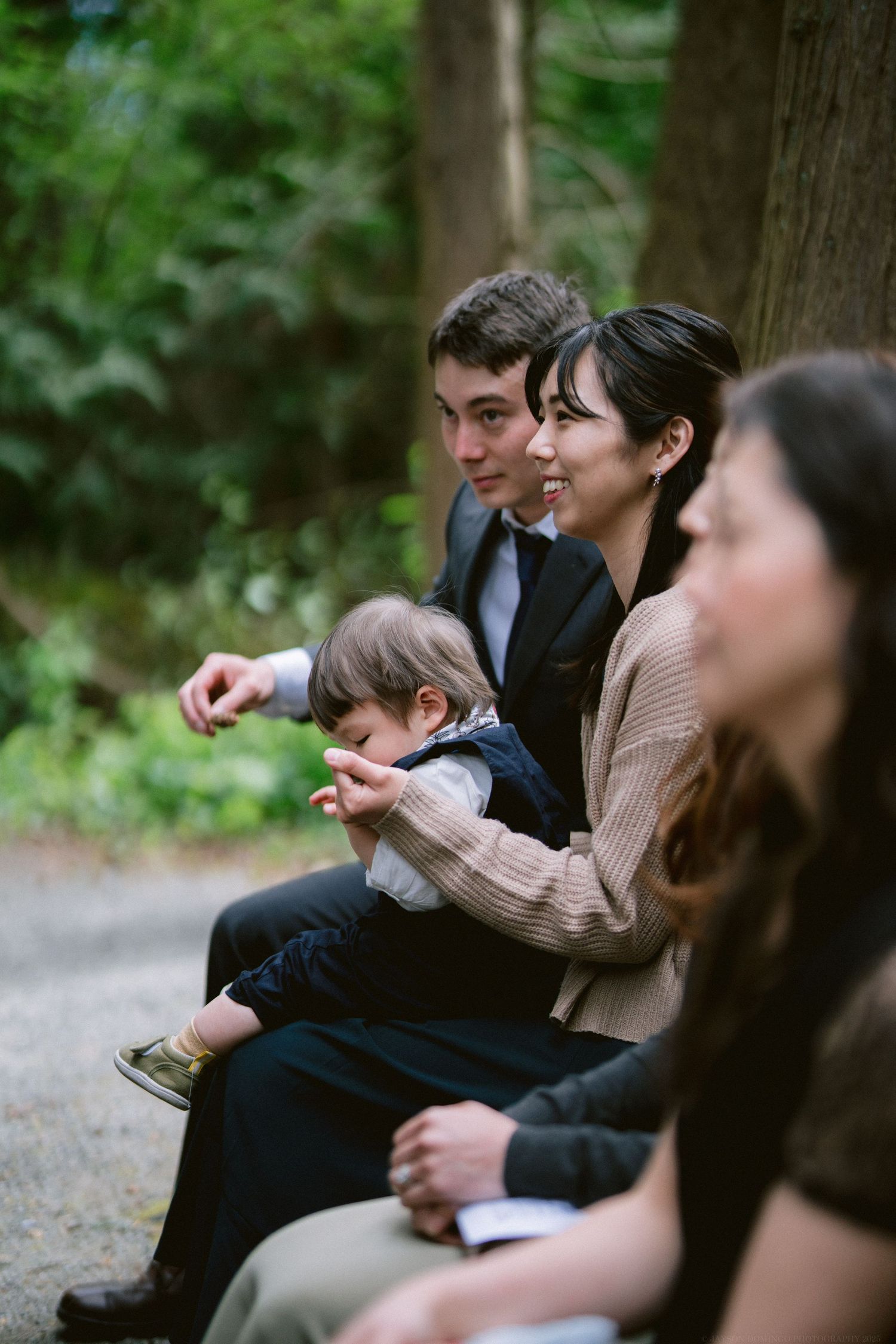 A relaxed gathering of people sitting together on a path in a wooded area with natural lighting.
