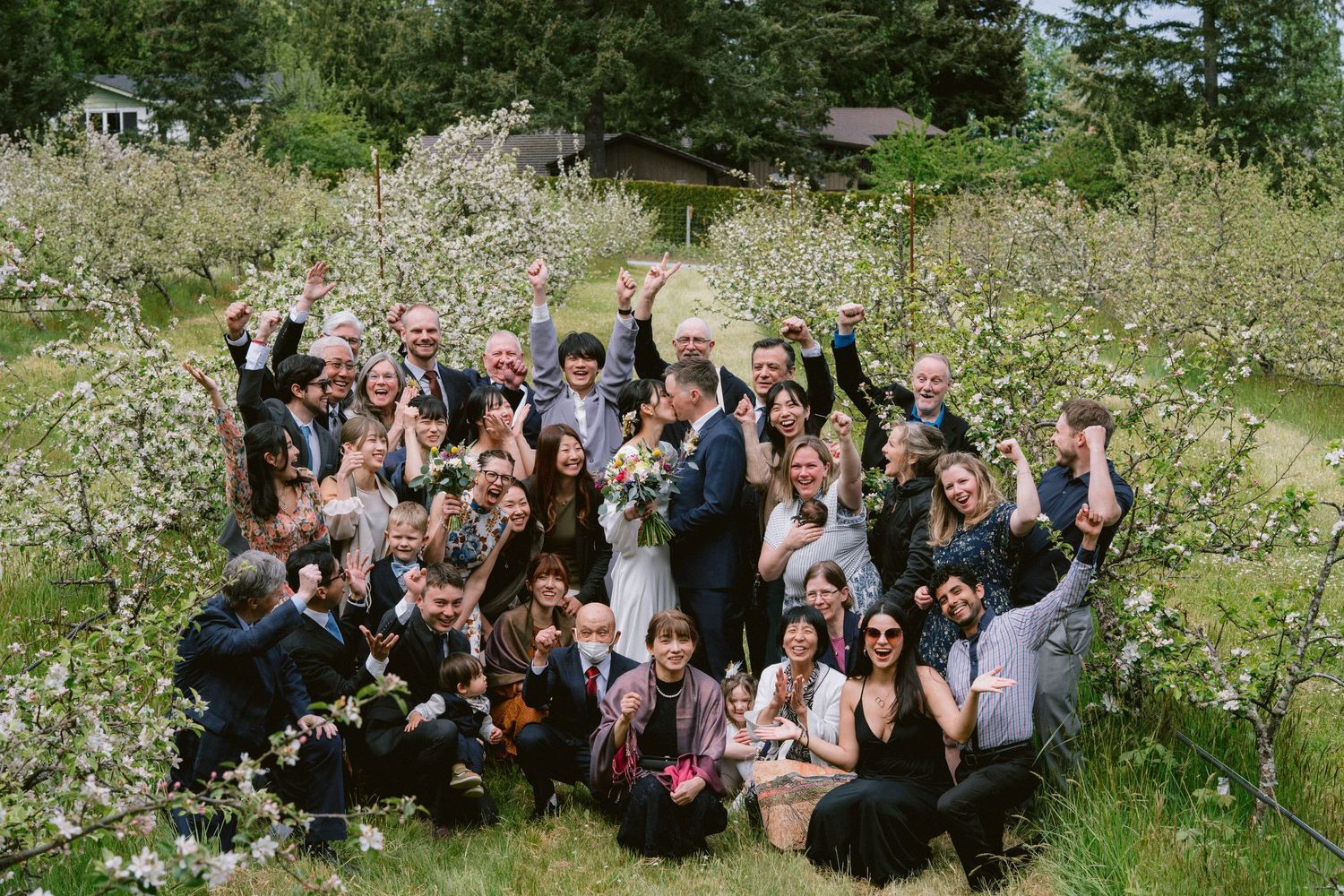 A large group celebrates outdoors in a meadow filled with wildflowers on a sunny day.