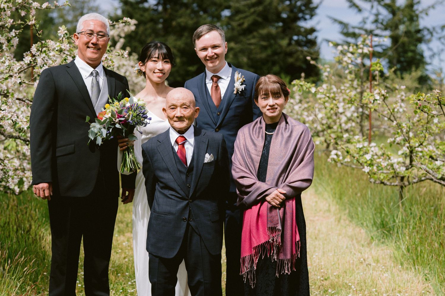 A group of people posing together outdoors on a spring day with blooming white flowers in the background.