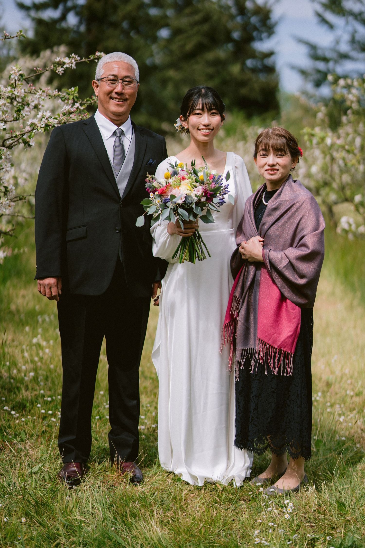 Wedding party poses together in formal attire with spring blossoms and greenery in the background.
