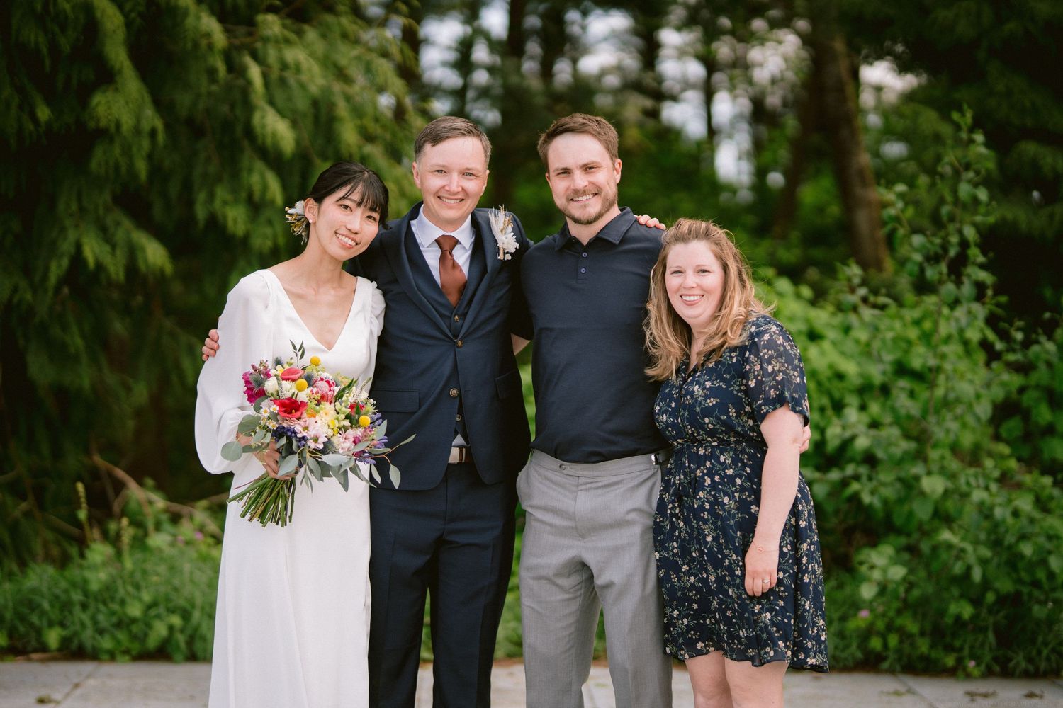 Wedding group poses together on path with greenery and colorful bouquet in Pacific Northwest setting.