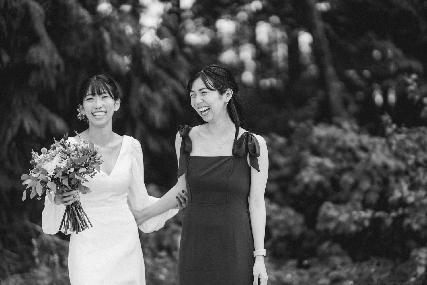 Two women share a joyful moment at a wedding, with one in white holding a vibrant bouquet.