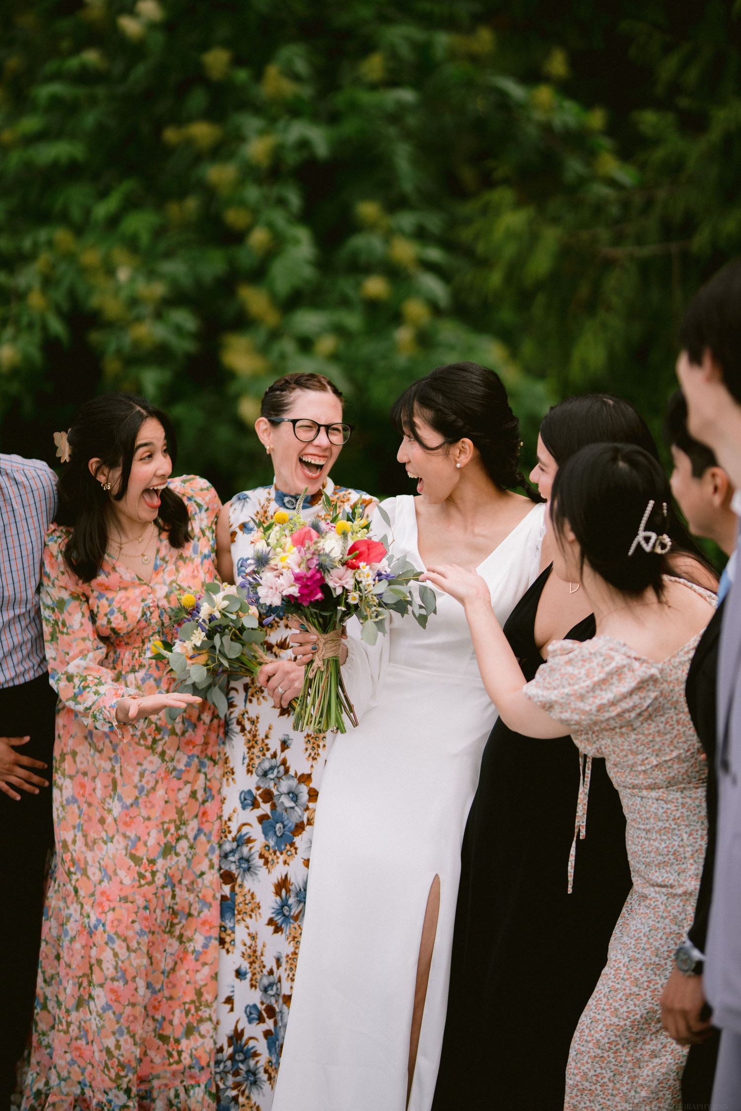 A joyful group shares laughter and embraces during wedding celebrations in a garden setting.
