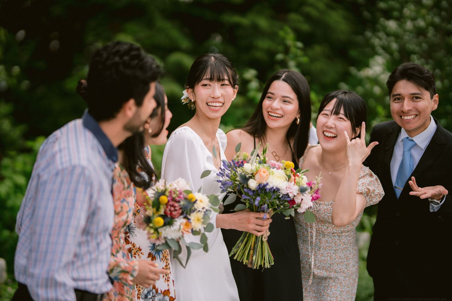 Wedding guests gather outdoors sharing joyful moments while holding vibrant floral bouquets.