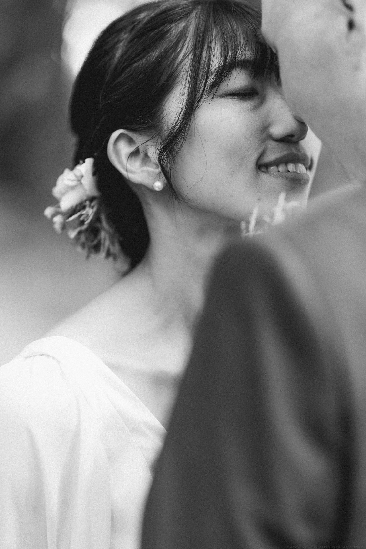 A black and white portrait of a bride with bangs smiling joyfully on her wedding day.