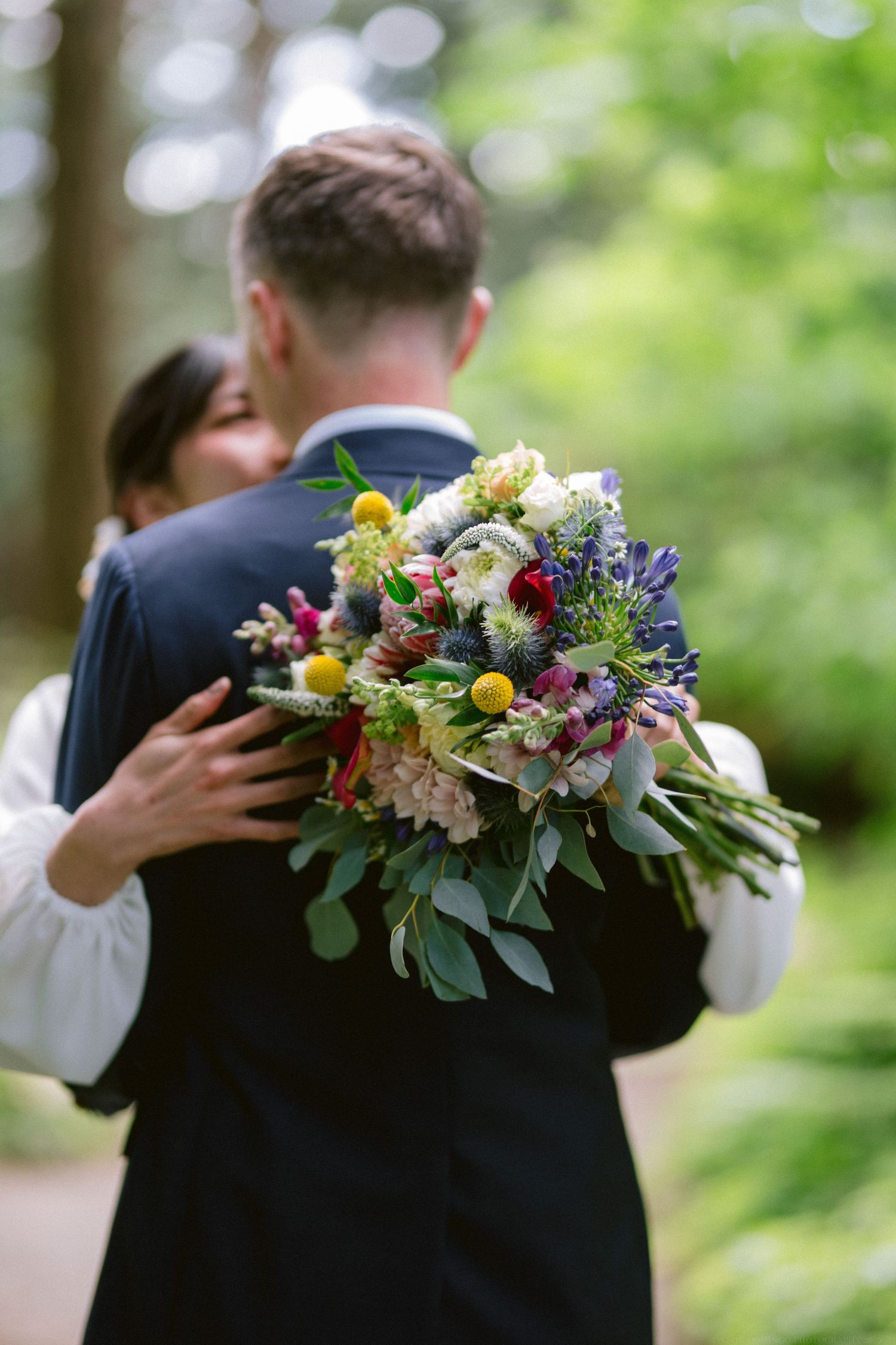 Close-up of a vibrant wildflower wedding bouquet held by someone in formal attire.
