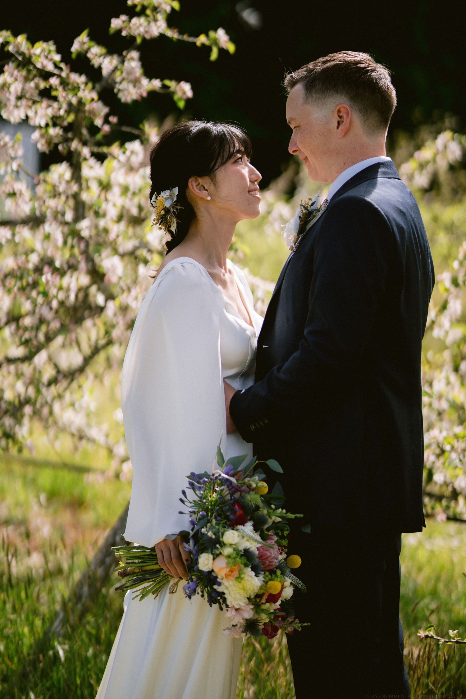 A romantic wedding portrait of a couple standing close together among blooming spring trees.