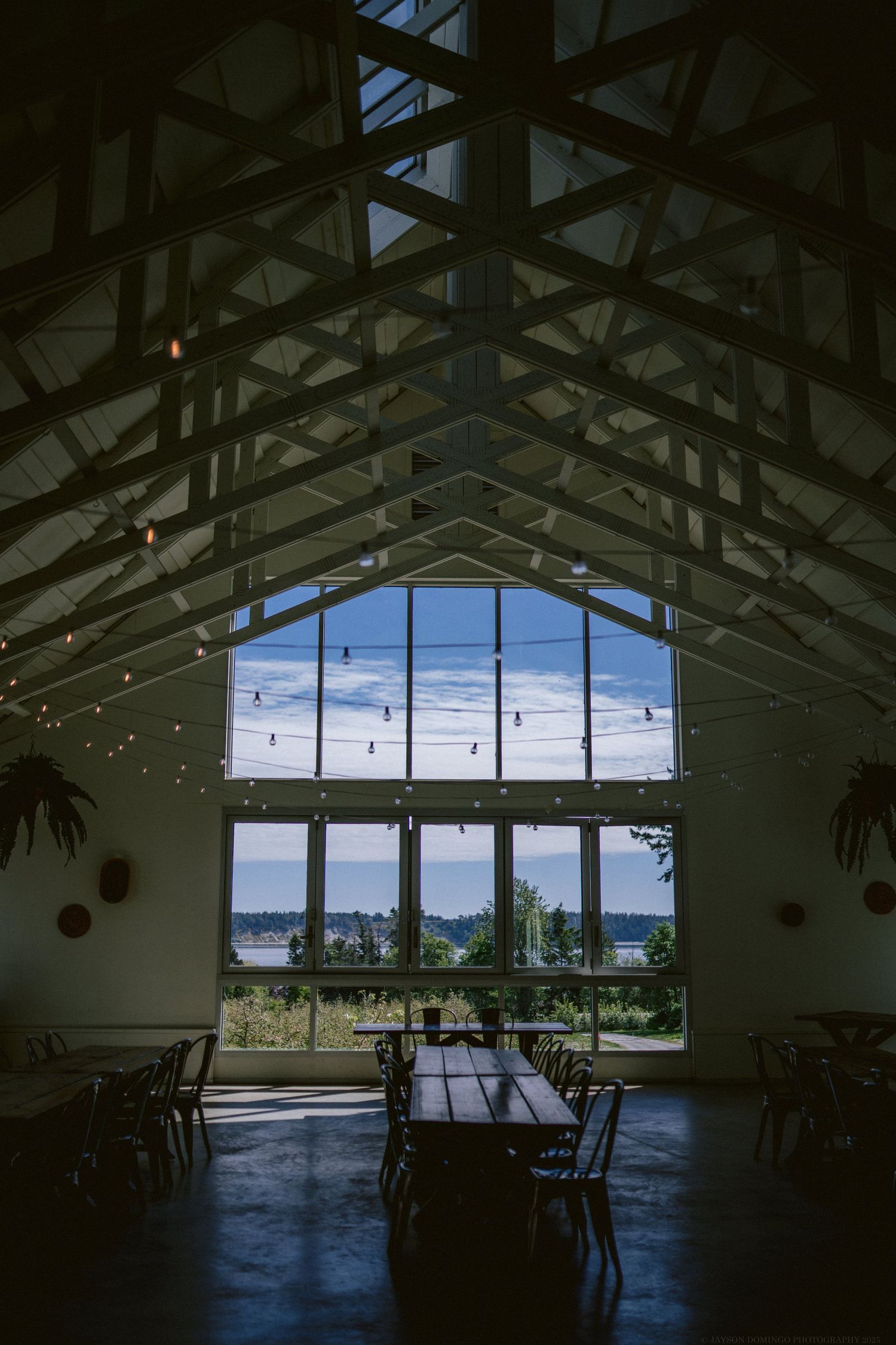Interior view of a grand reception hall with vaulted wooden beams and large windows overlooking a waterfront view.