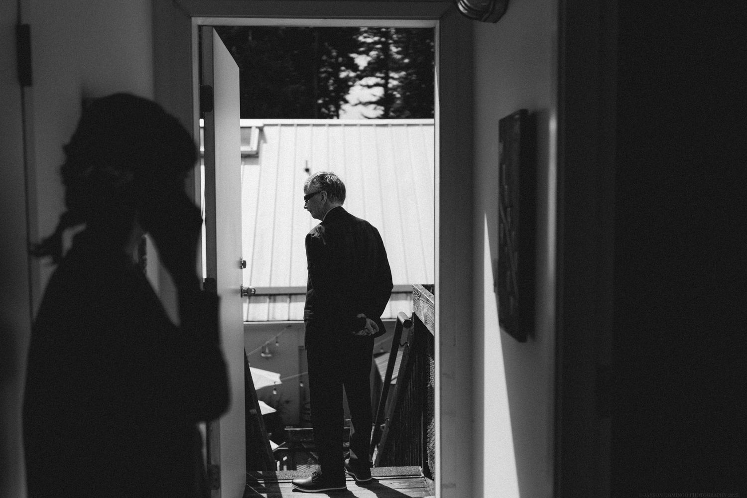 Black and white silhouette of a person standing in a doorway with dramatic shadows on the walls.