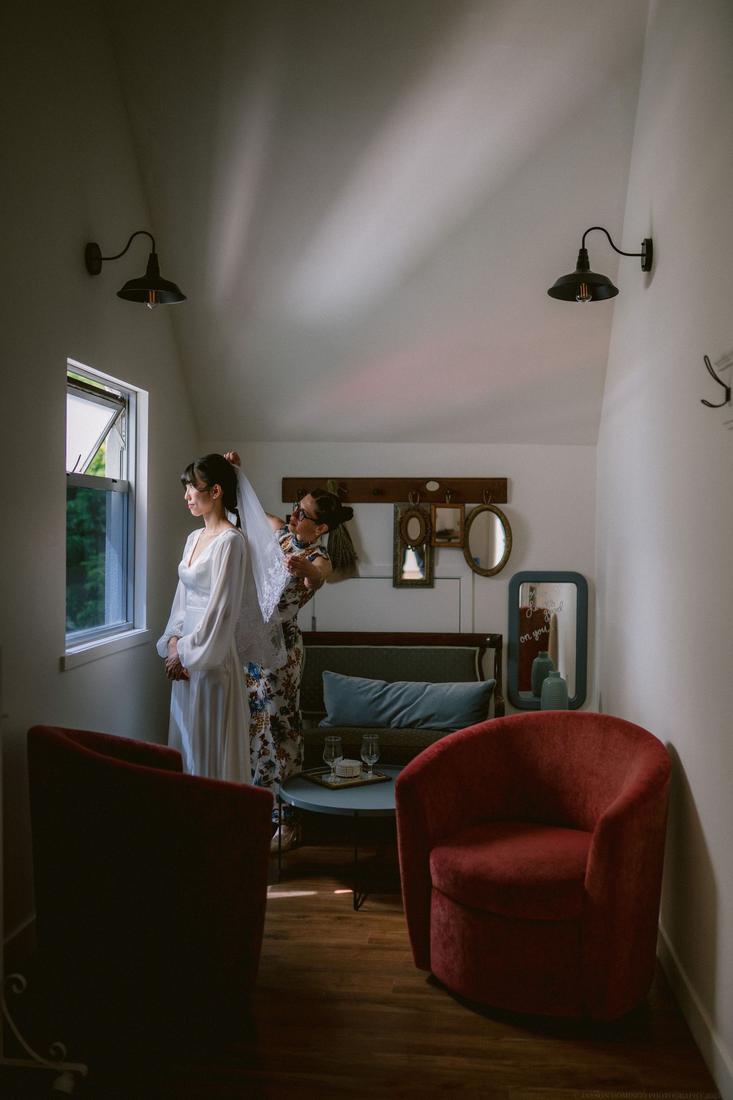 Getting ready room with vintage decor featuring a red velvet chair, window light, and wall sconces.