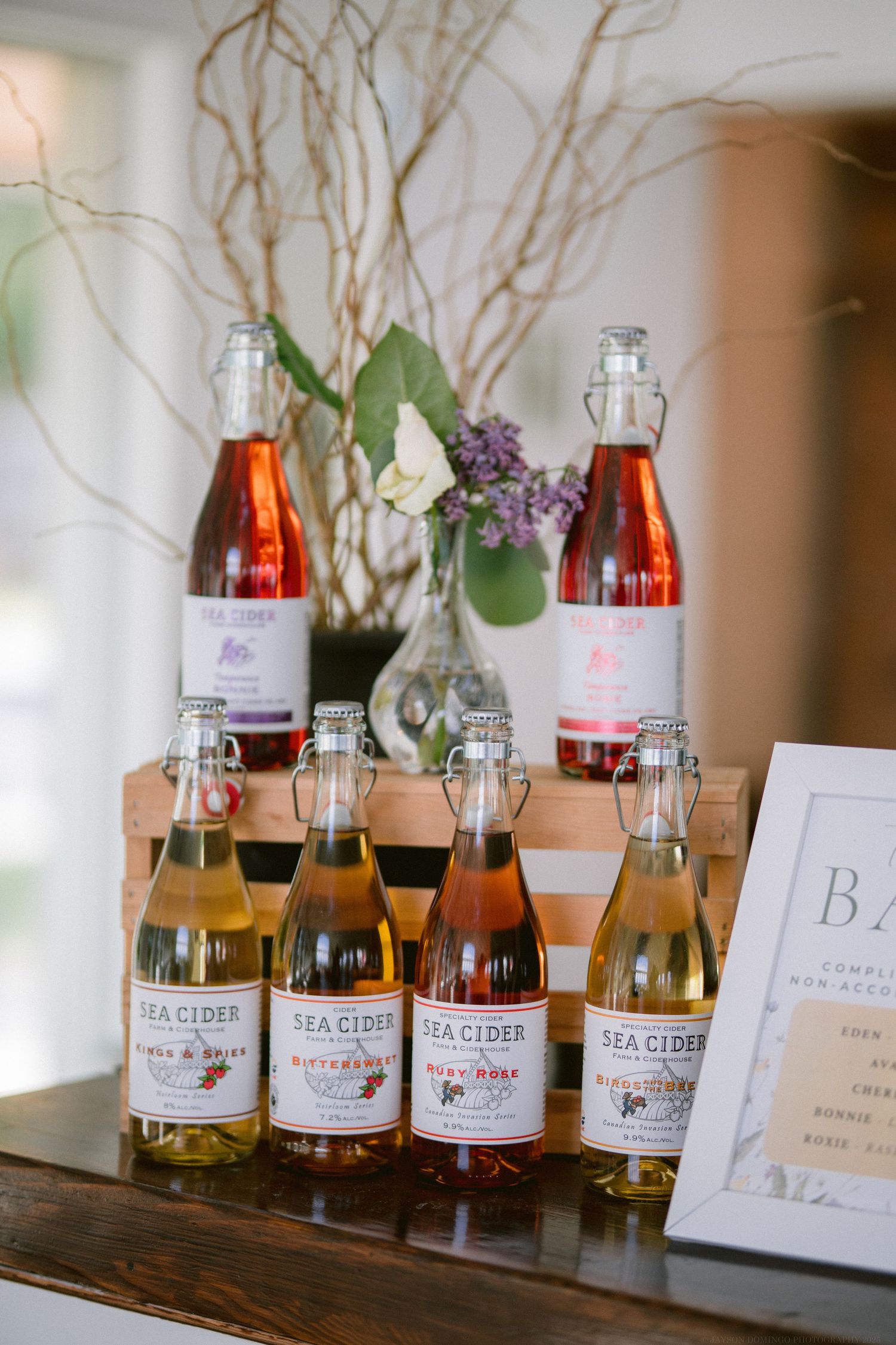 Display of Sea Cider bottles and branches arranged on wooden surface with event signage.