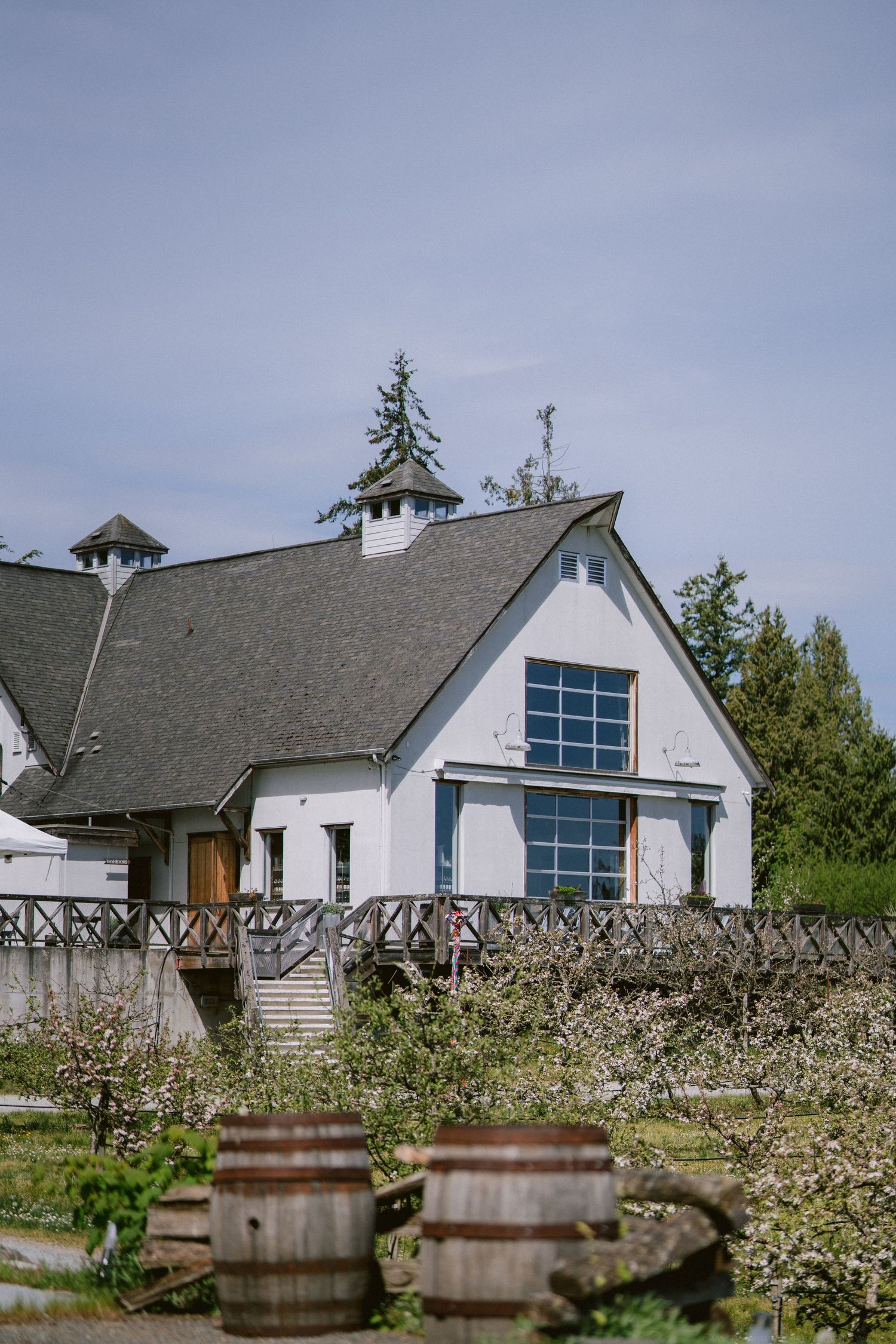 White rustic barn-style wedding venue with grey roof and wooden barrels in the foreground.