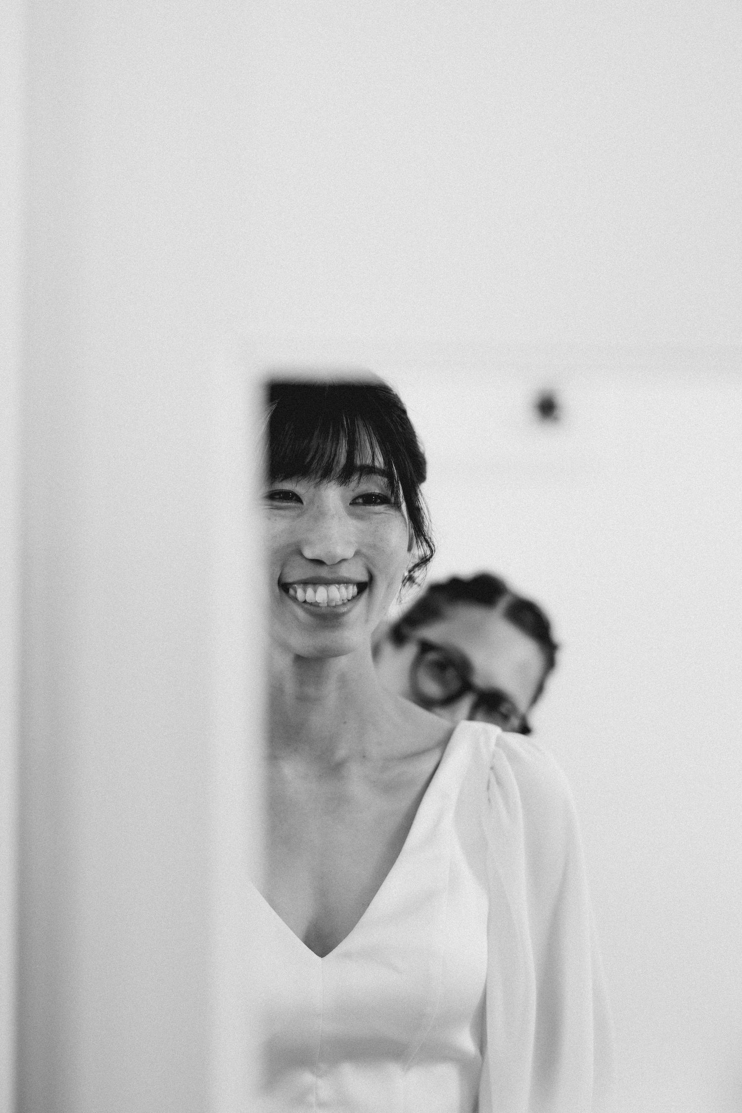 A reflection captured in a mirror showing two people in a bright white room.