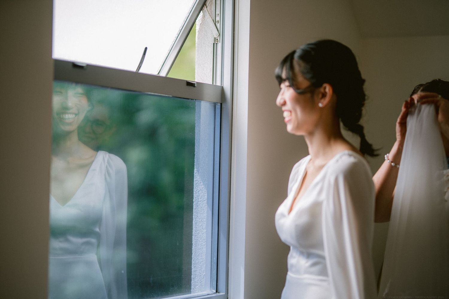 Person in white dress standing by window with soft natural light filtering through.