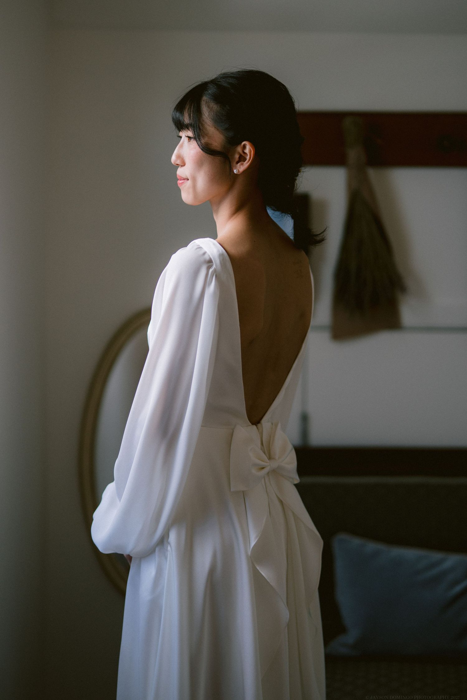 Side profile of someone wearing an elegant white backless dress with billowing sleeves and a delicate bow detail.