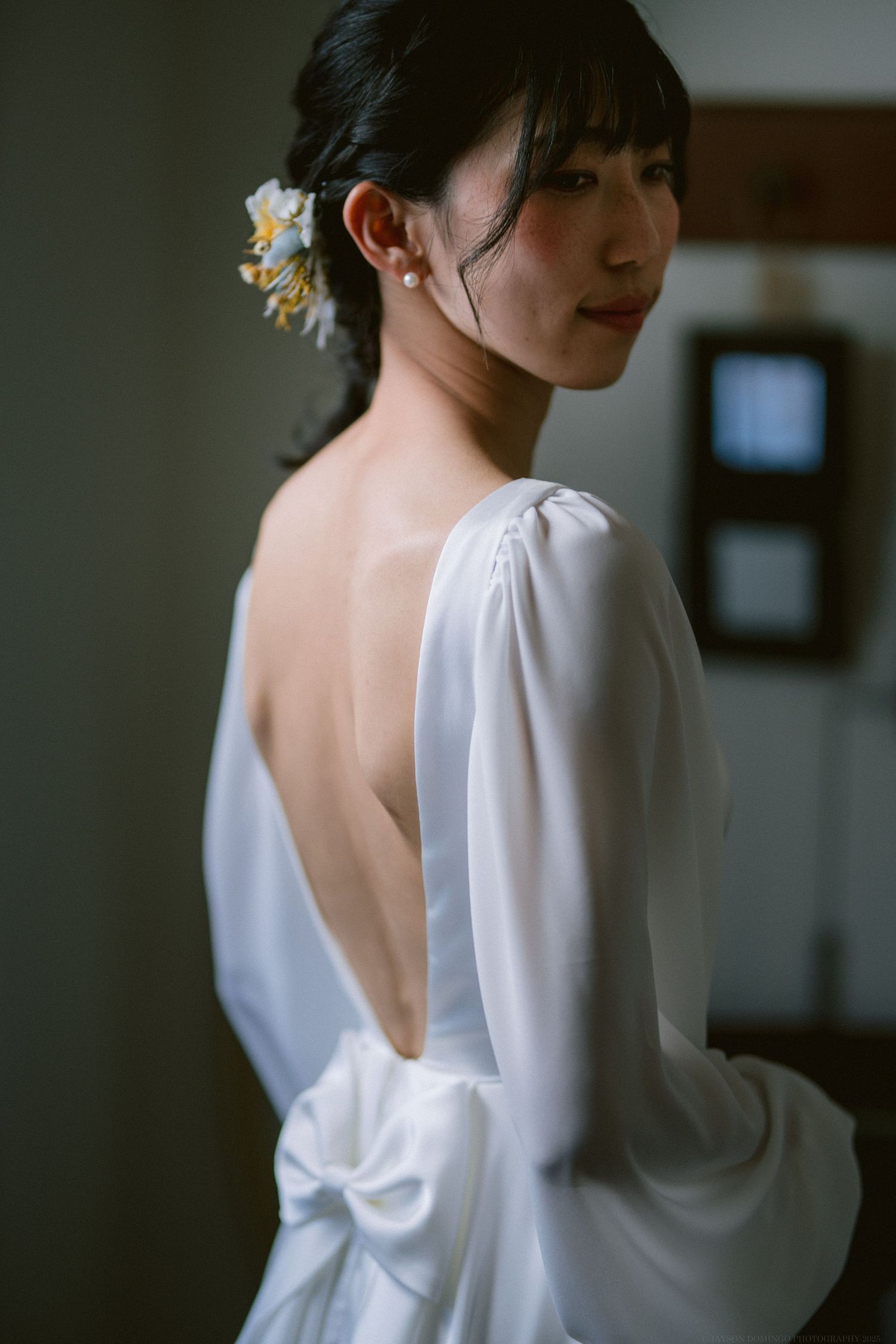 Elegant open-back white dress with long sleeves and delicate floral hair accessory shown from behind.