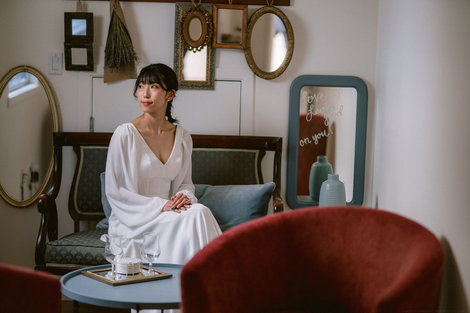 Vintage-style room interior with multiple mirrors and red velvet chair against white walls.