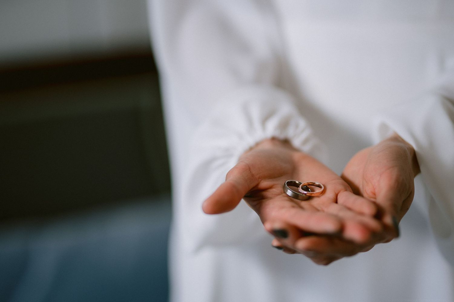 Close up of hands holding wedding rings against a white sleeve background.