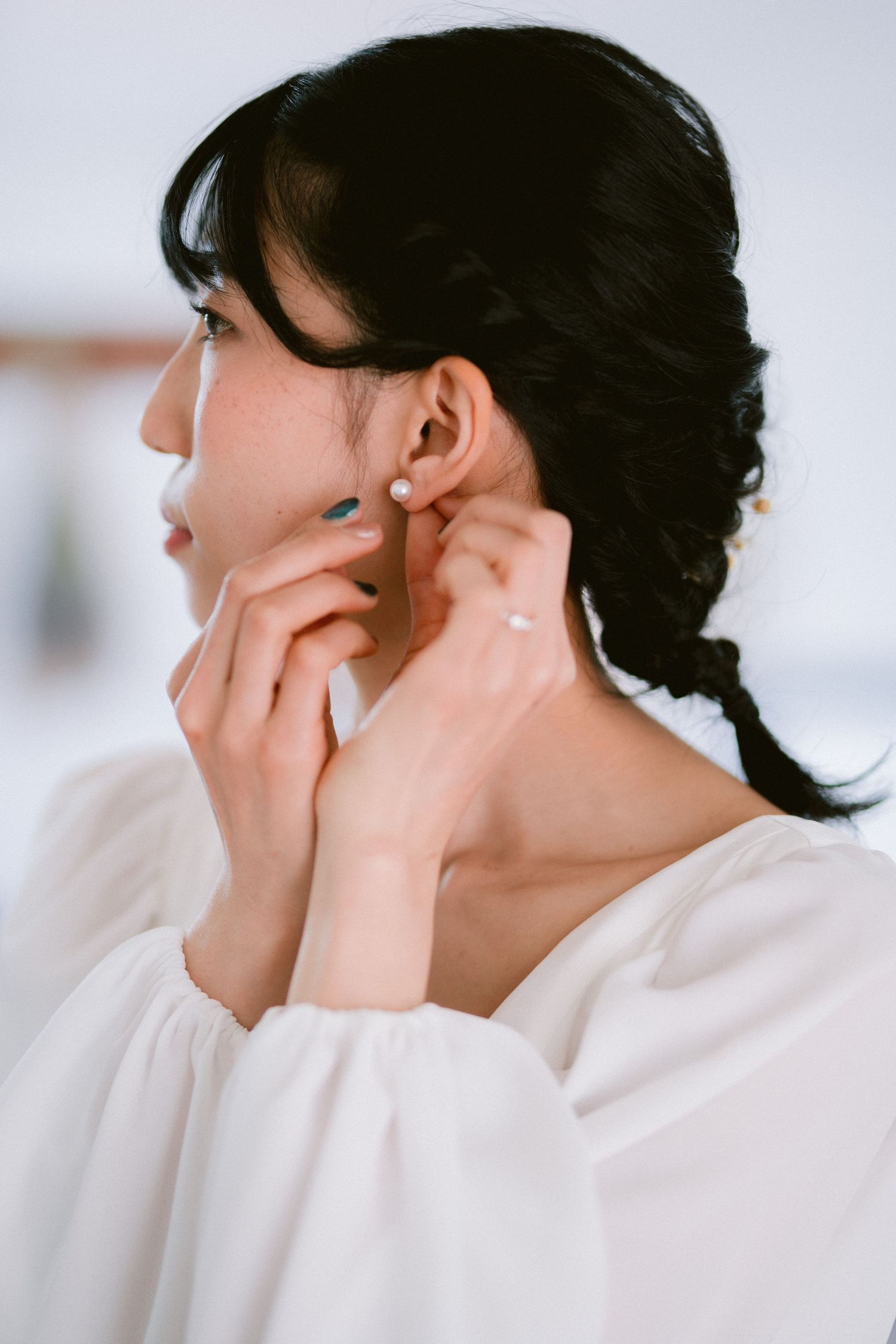 Side profile of someone with black hair in a white blouse delicately touching their ear.