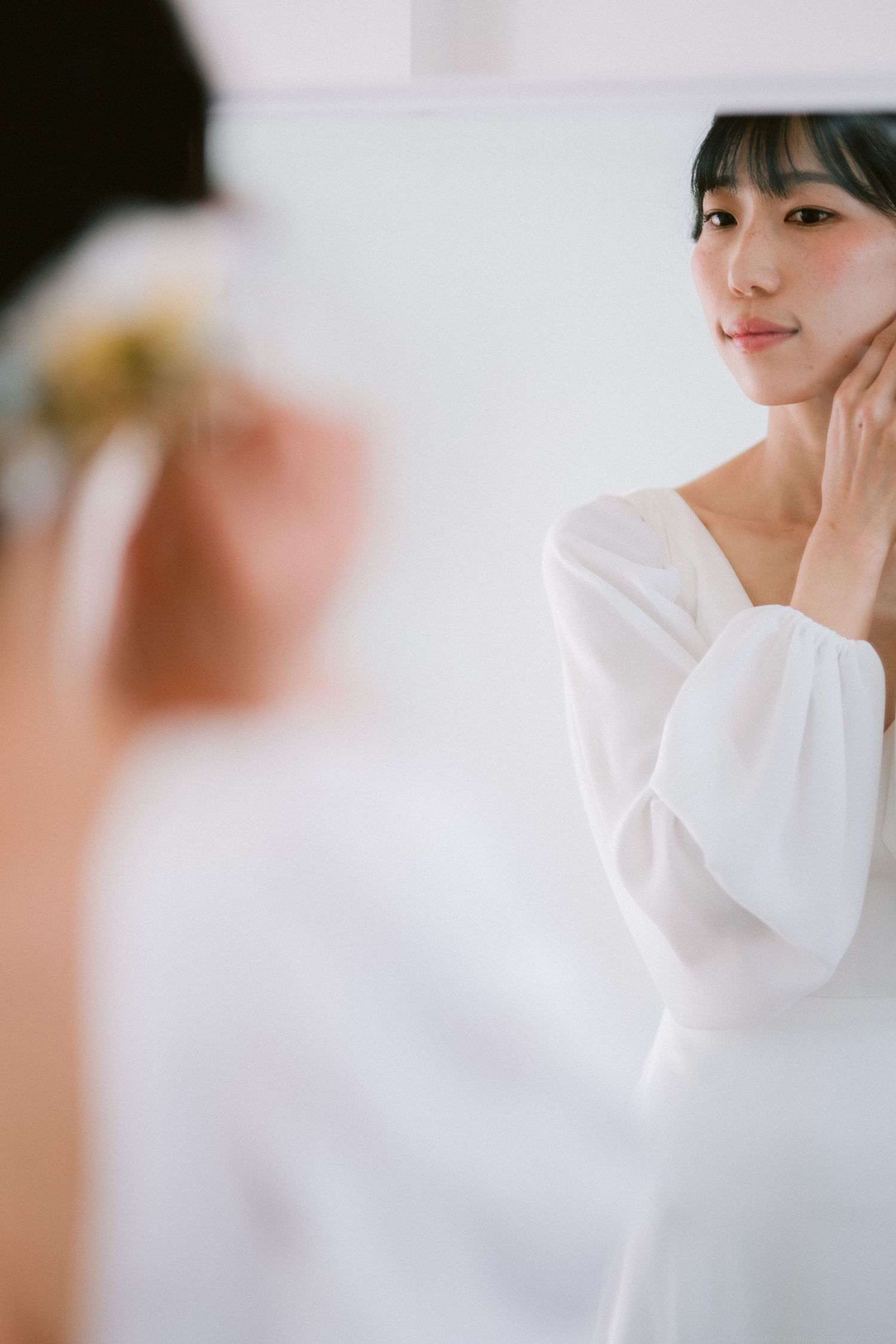 Soft focus mirror reflection showing white dress and gentle hand gesture.