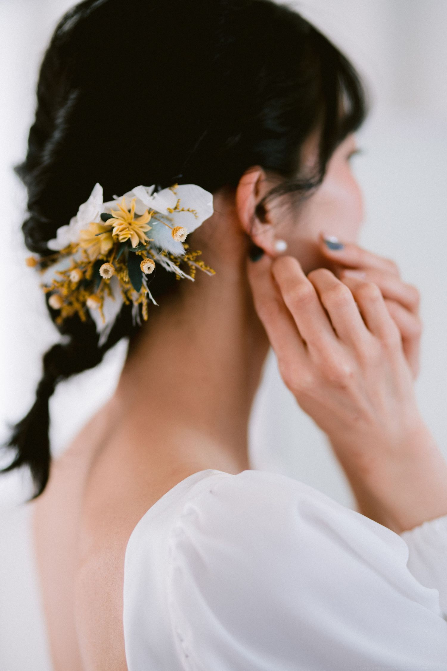Beautiful yellow flower hair accessory adorns dark braided hair against white clothing in romantic bridal style.