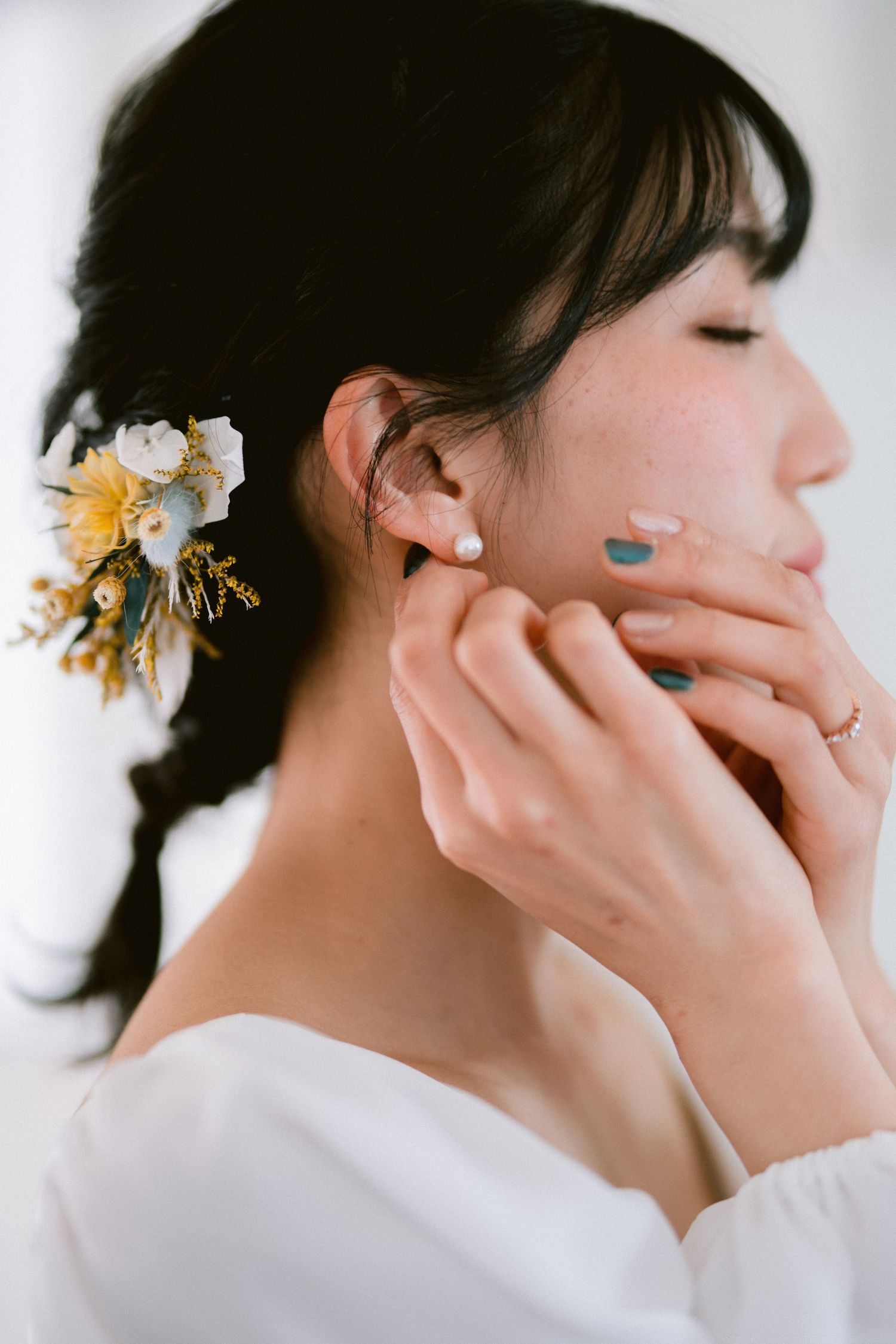 Close-up profile view showing white floral hair accessory, pearl earring, and delicate hand placement.