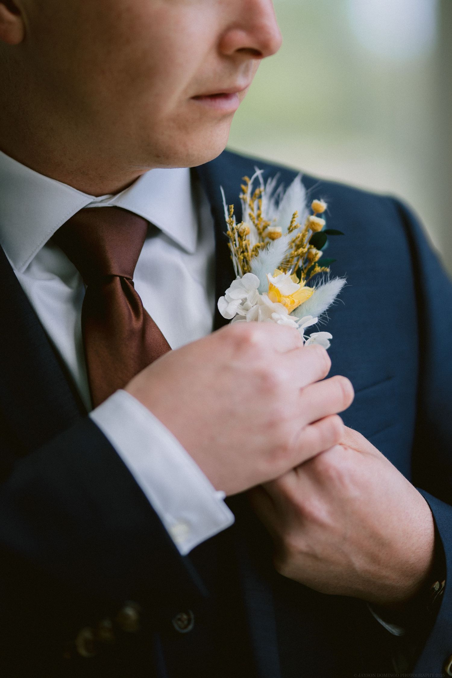 Close-up of wedding boutonniere with dried flowers on navy suit jacket with brown tie.