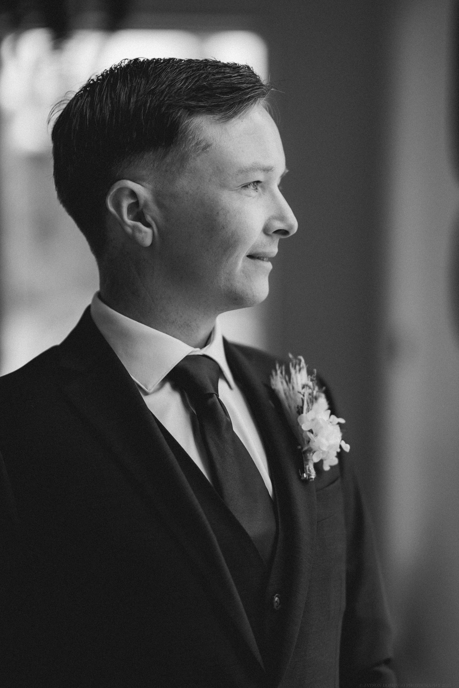 Black and white profile portrait of a groom in a classic three-piece suit with boutonniere at a wedding.