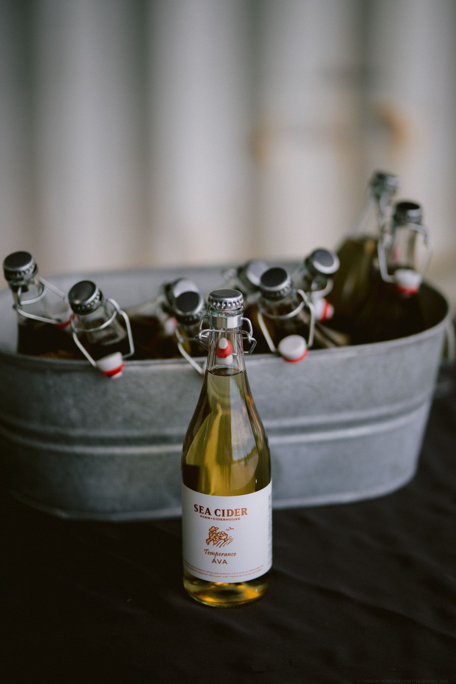 A Sea Cider bottle stands in front of a galvanized metal tub filled with other beverages.