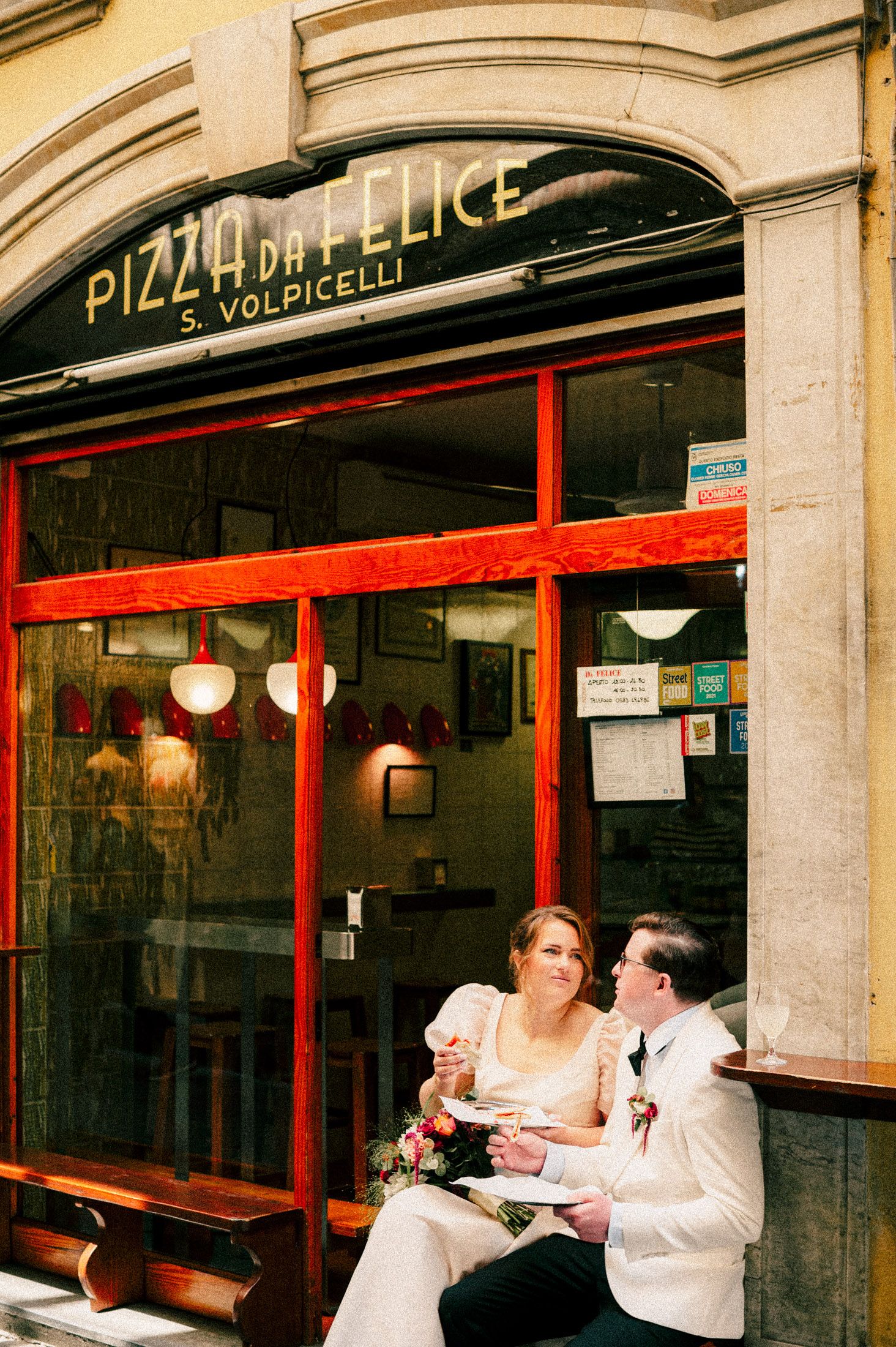 Couple dining outside Pizza Felice restaurant in vintage-style setting.