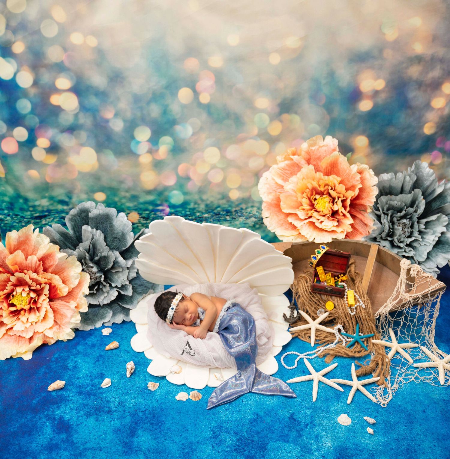 Coastal themed newborn setup with seashells, flowers and starfish on blue backdrop.