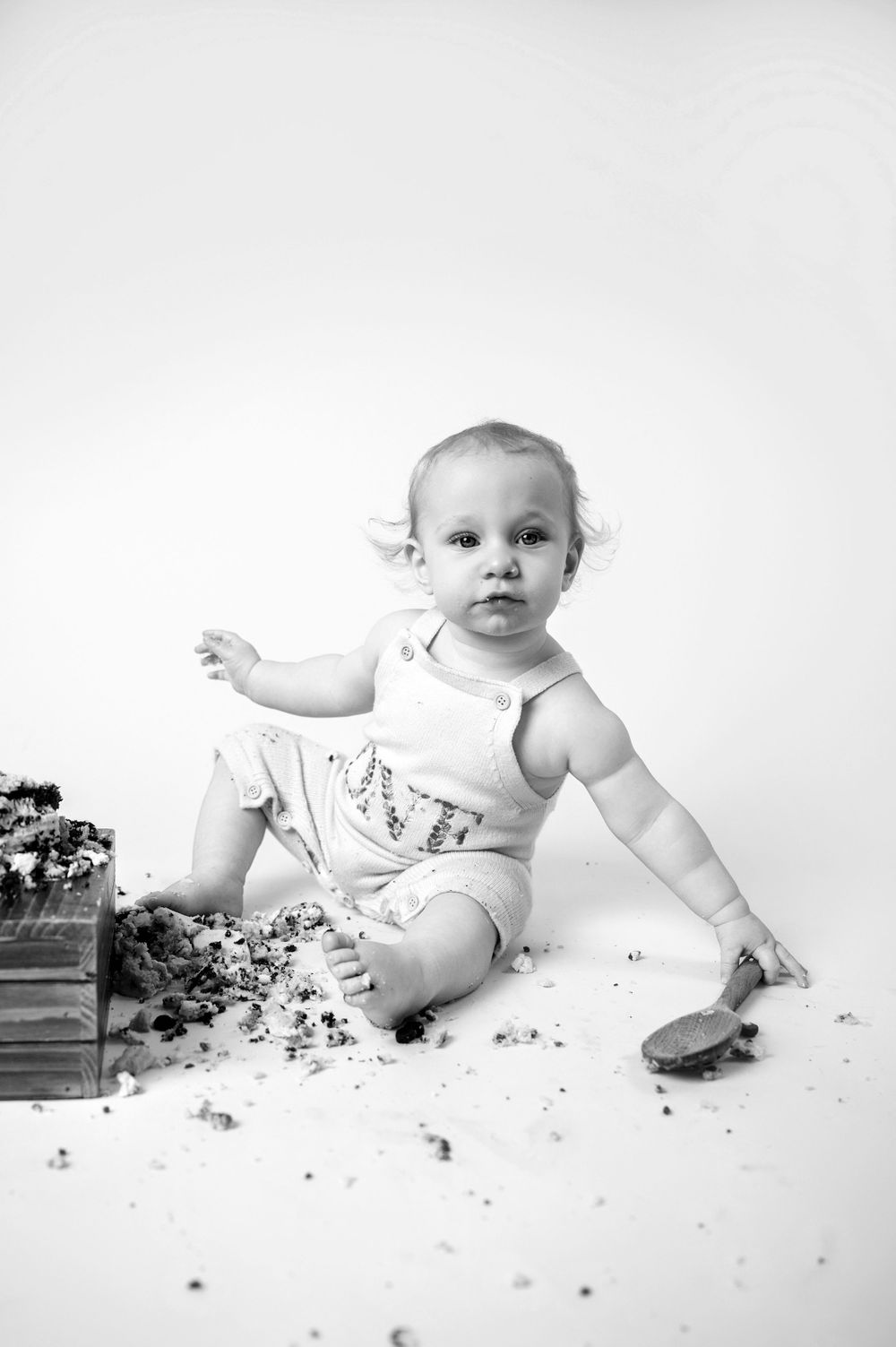 Sweet black and white portrait of baby sitting with cake smear and messy crumbs in studio setting.