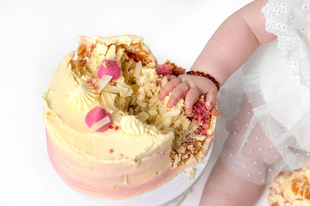 Small hand reaching for pink and yellow cake with rose petals.