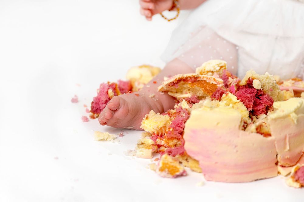 Pink macaron cookies with scattered crumbs and decorative edible powder on a white surface.
