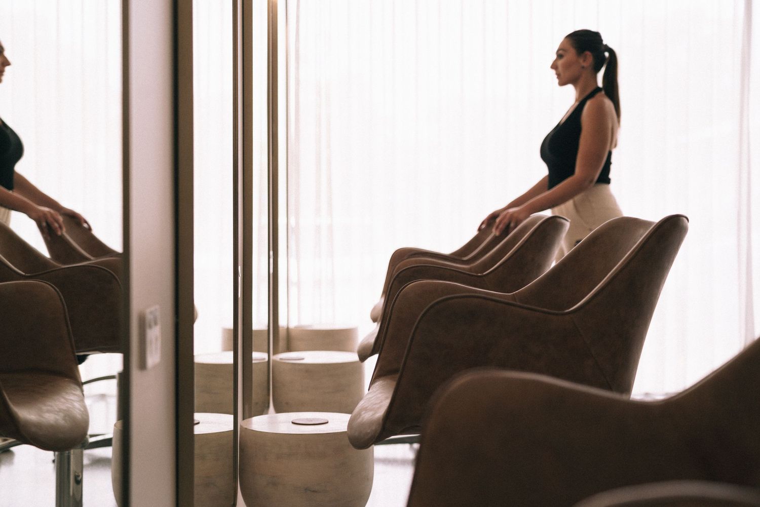 Person sitting in brown chair in silhouette against window light in tranquil room setting.