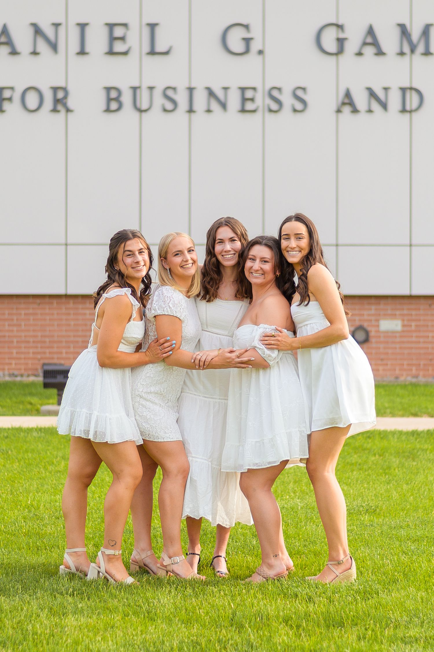 Group of graduates in white dresses posing together outside the Gambet Center for Business.