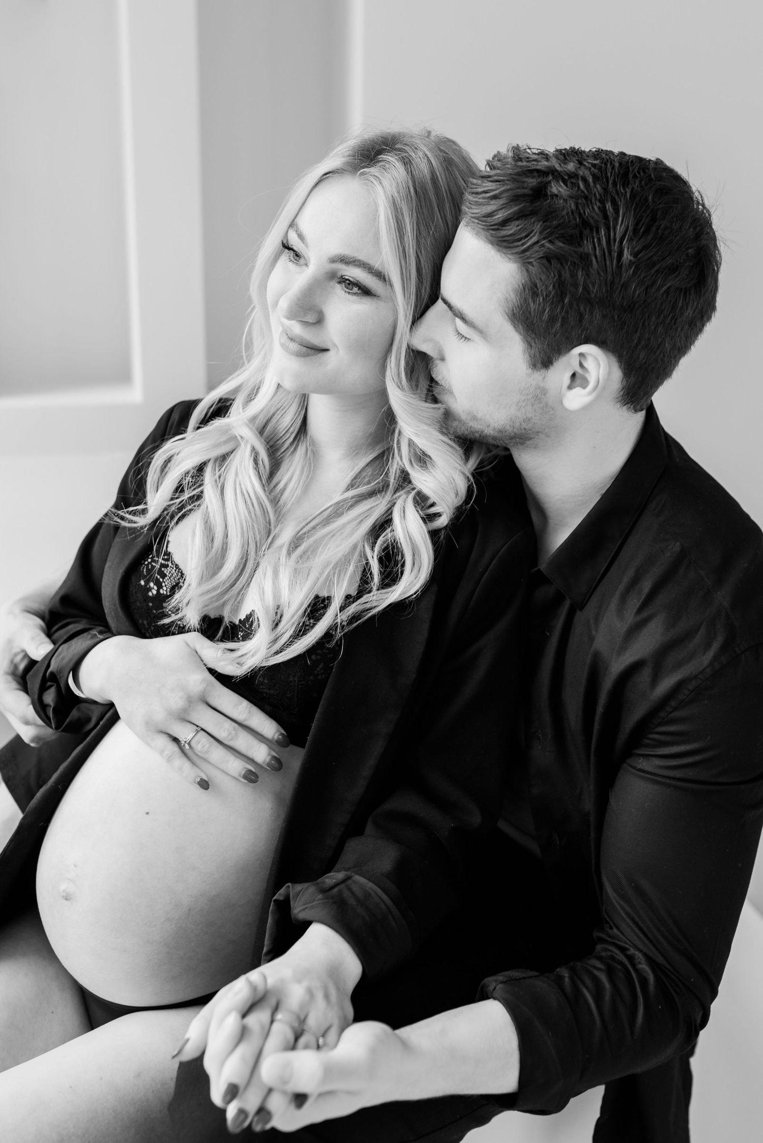 Black and white maternity photo of a couple in dark clothing sharing an intimate moment together.