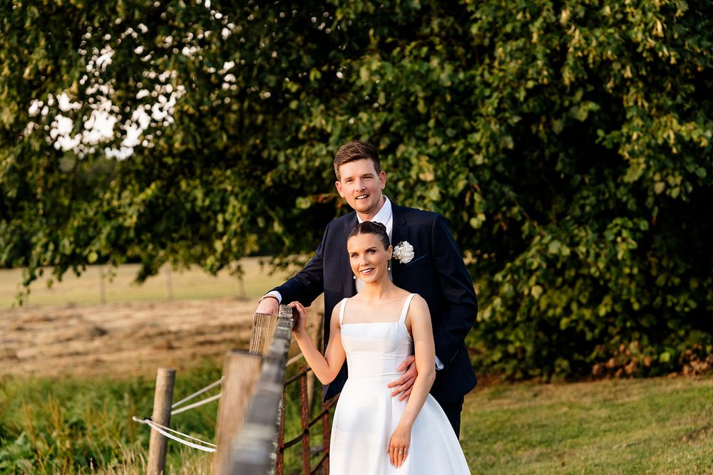Two people in formal wedding attire walk together through a garden setting during an outdoor ceremony.