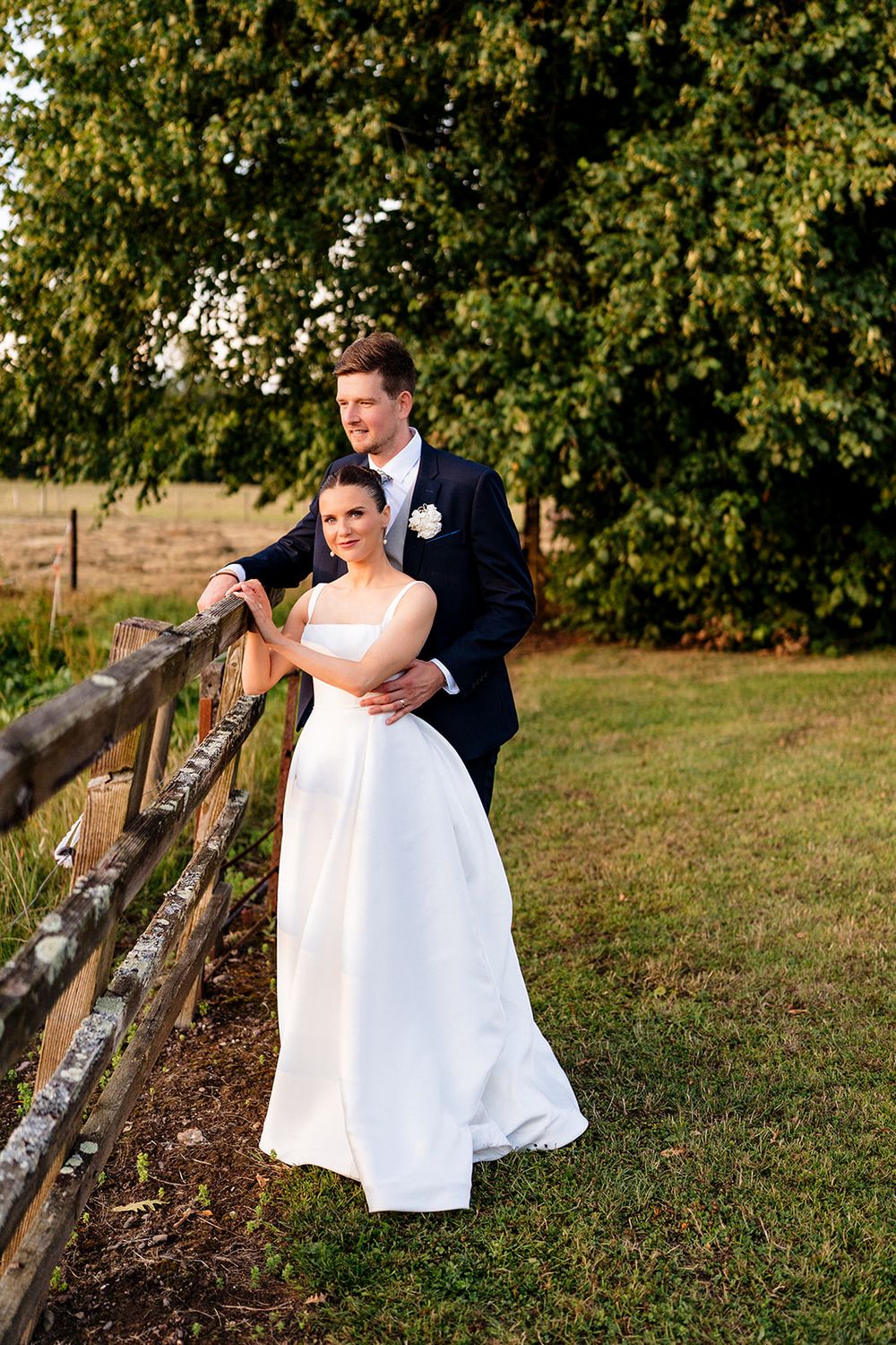 A romantic moment between a couple in wedding attire near a rustic wooden fence at sunset.