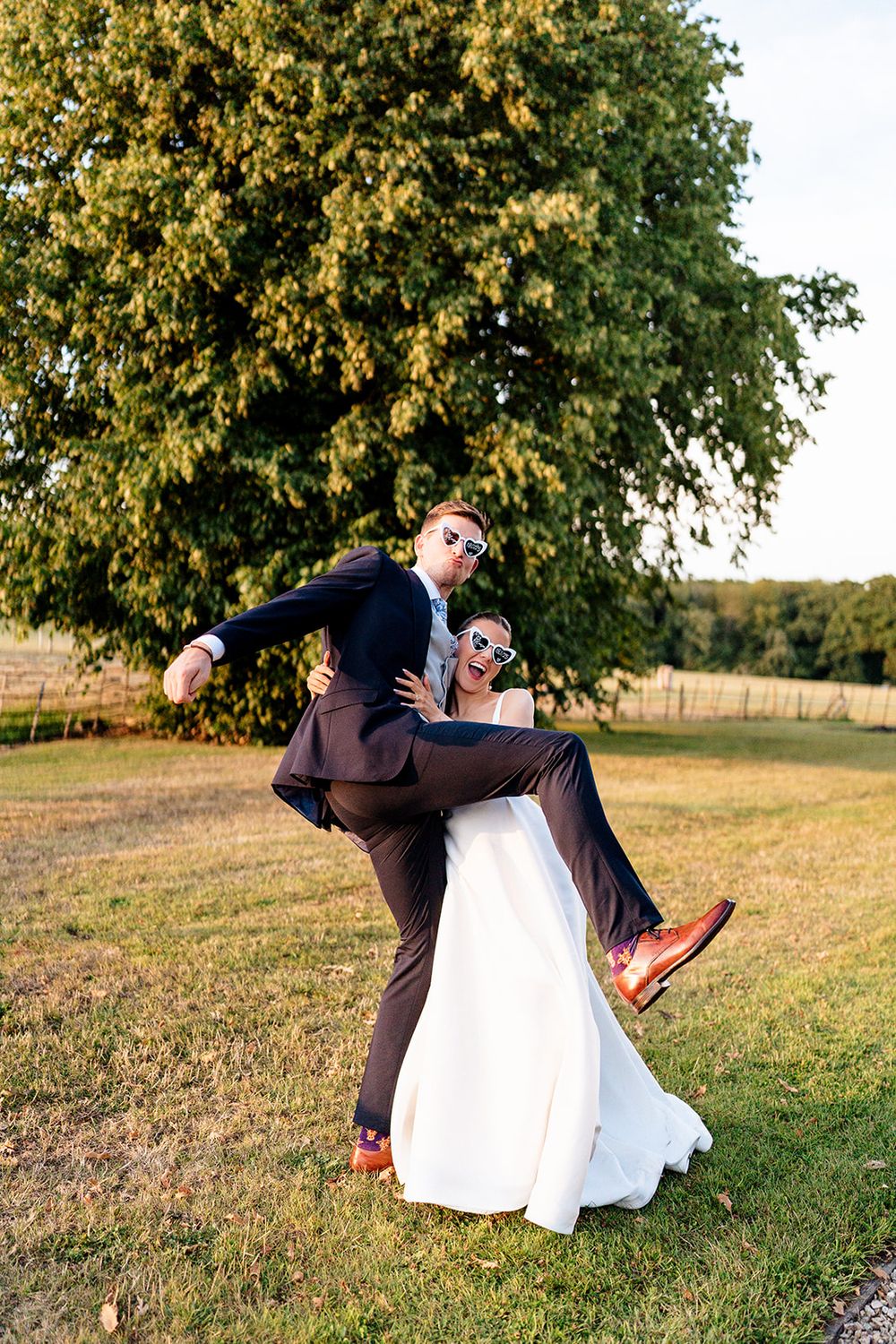 A romantic dip pose between a couple in wedding attire on a grassy hill during golden hour sunset.